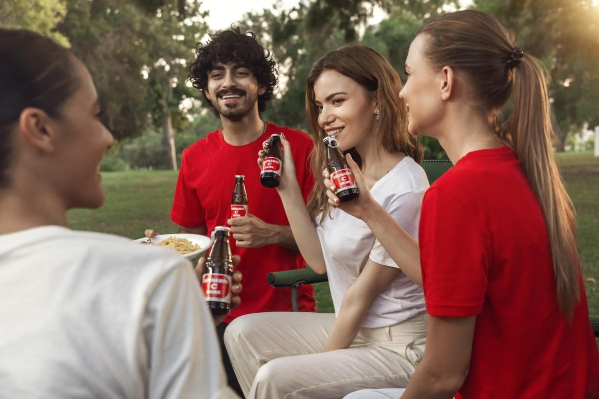 Lifestyle brand photography of friends socializing outdoors, holding bottled drinks in a park setting with natural light and relaxed energy